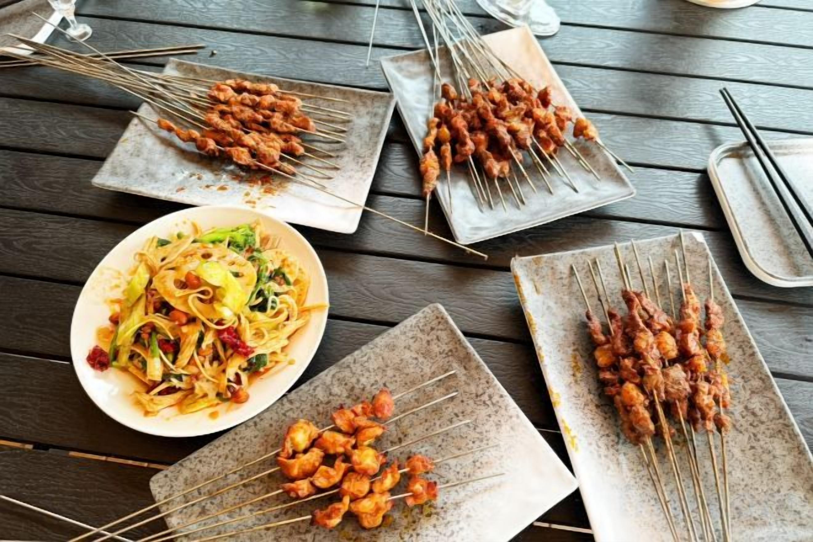 A dining table with skewers of grilled meat and a plate of noodles.