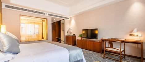 Quarto de hotel com cama, escrivaninha, cadeira, televisão e uma janela grande.