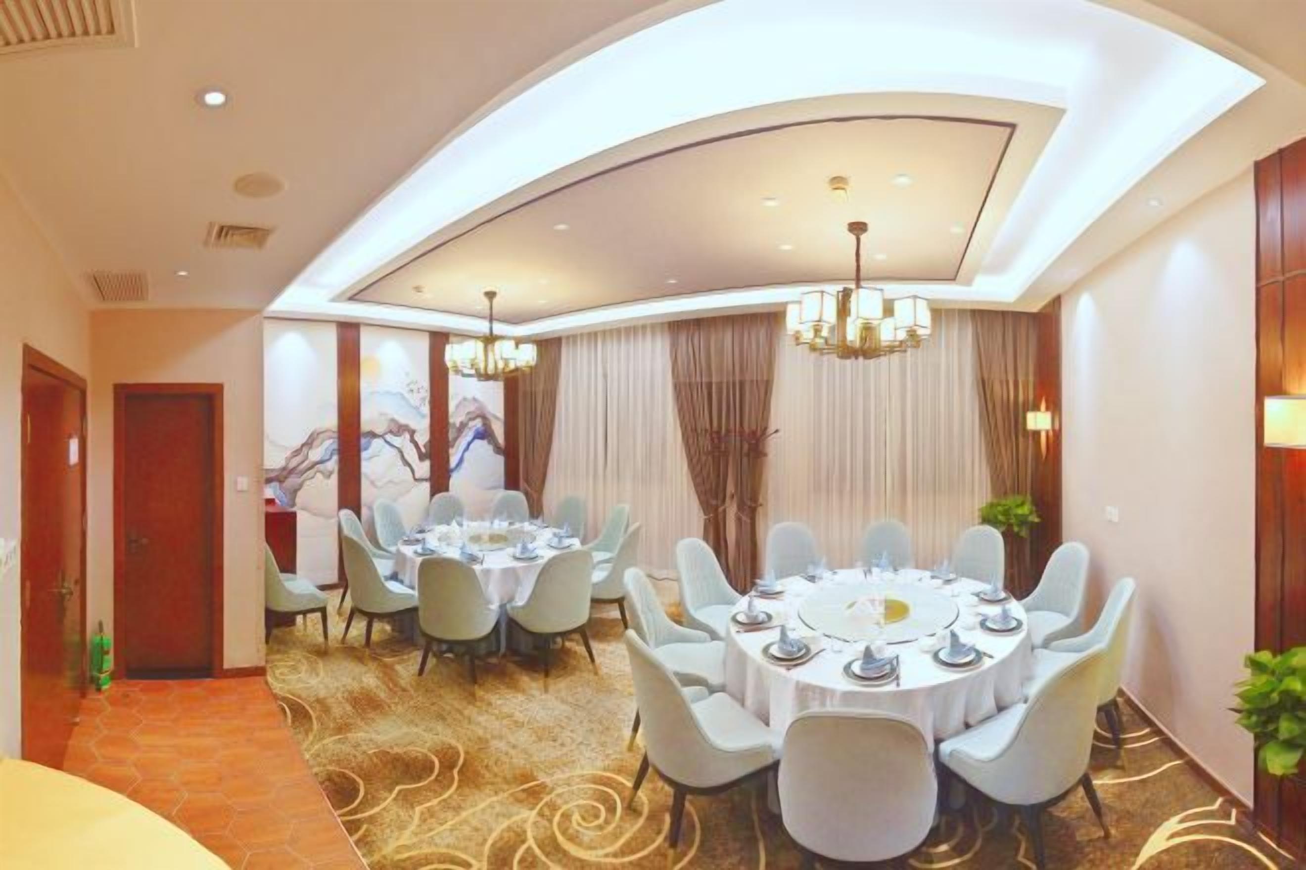 A hotel dining room with round tables, chairs, and a chandelier.