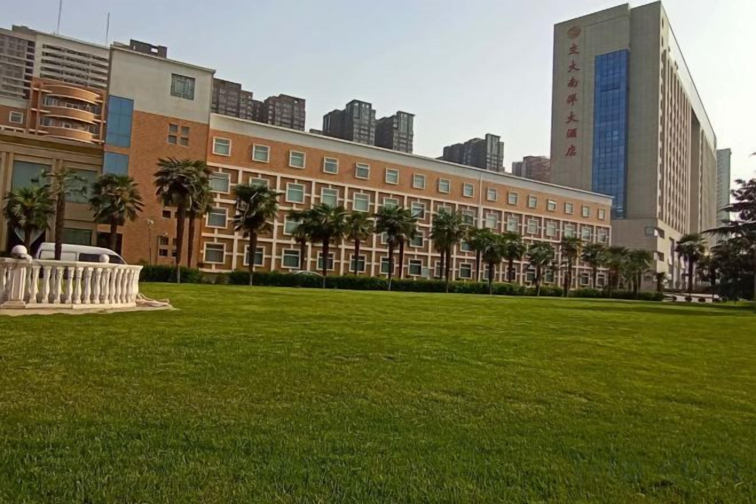 A hotel with a large grassy courtyard, multiple floors, and a tall building with a blue glass facade.