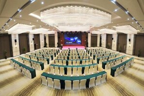 Een ruime congreszaal met een podium aan de voorzijde en zitplaatsen in meerdere rijen.
