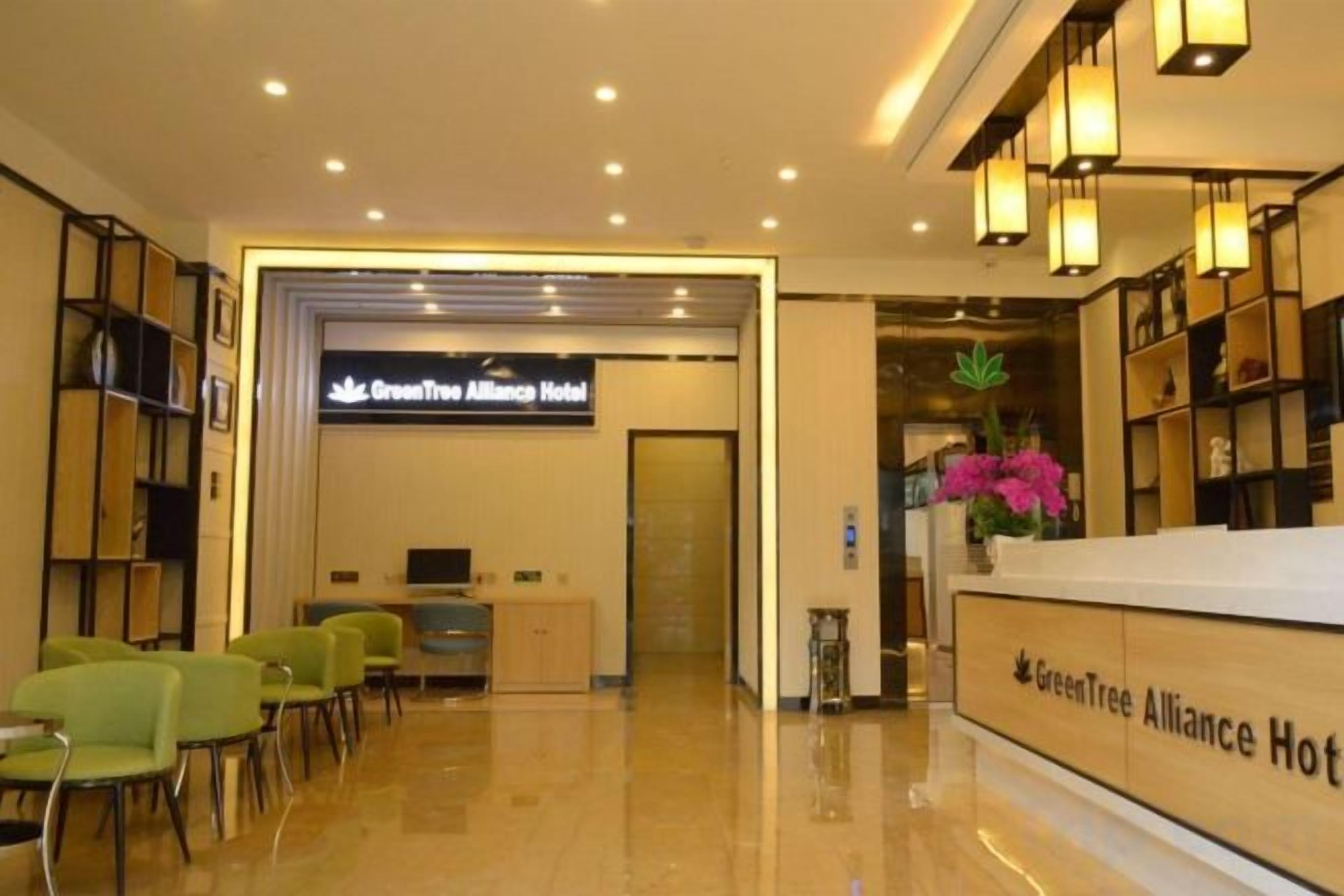 A hotel reception area with a reception desk, chairs, and a sign for the GreenTree Alliance Hotel.