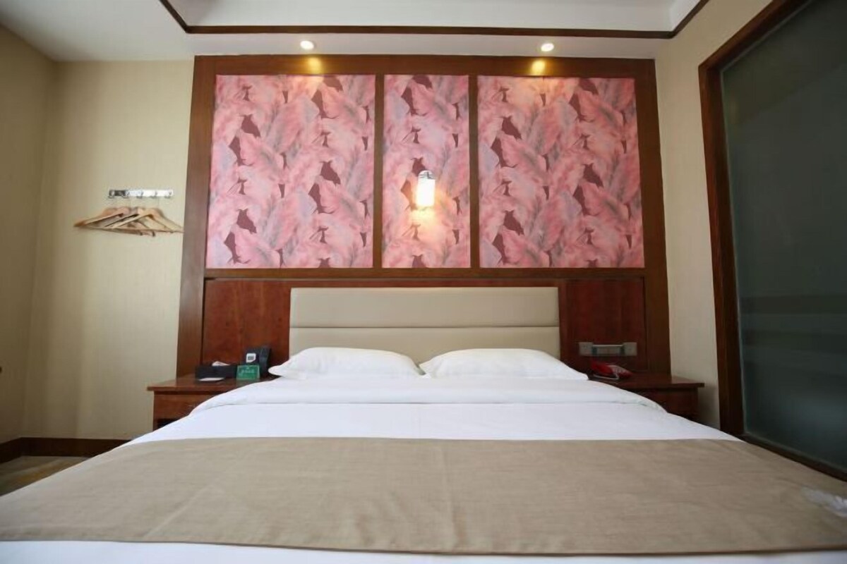 A hotel room with a large bed, a wooden headboard, a nightstand, and a wall-mounted light fixture.