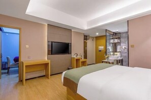 Hotellihuone, jossa on sänky, työpöytä, televisio, kylpyhuone, jossa on peili ja pesuallas, sekä vaatekaappi.