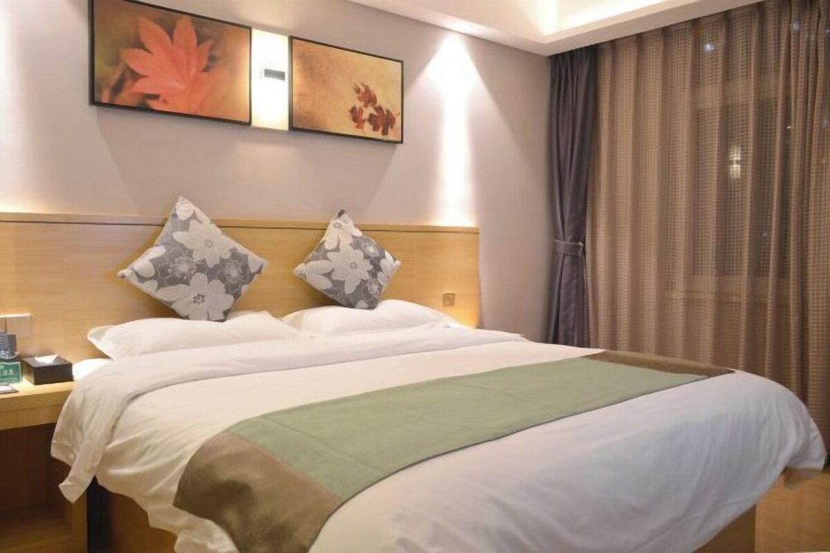 A neatly made bed with a green and white bedspread, two decorative pillows, and a wooden headboard.