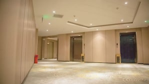 Corredor de hotel com paredes bege, carpete estampado e iluminação embutida.
