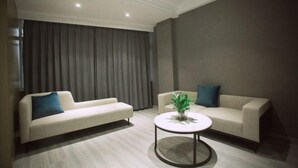 Uma sala de estar moderna com dois sofás, uma mesa de centro redonda e uma janela grande com cortinas.