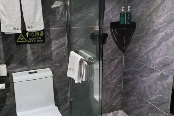 Casa de banho com chuveiro em cabine de vidro, sanita branca e prateleira preta com artigos de higiene pessoal.