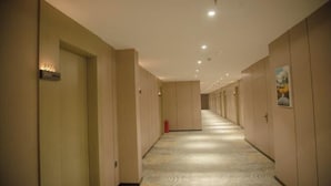 Corredor de hotel com portas em ambos os lados, carpete estampado e iluminação embutida no teto.