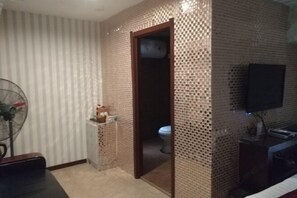 Un baño con pared de azulejos, un inodoro, un lavabo y un ventilador.