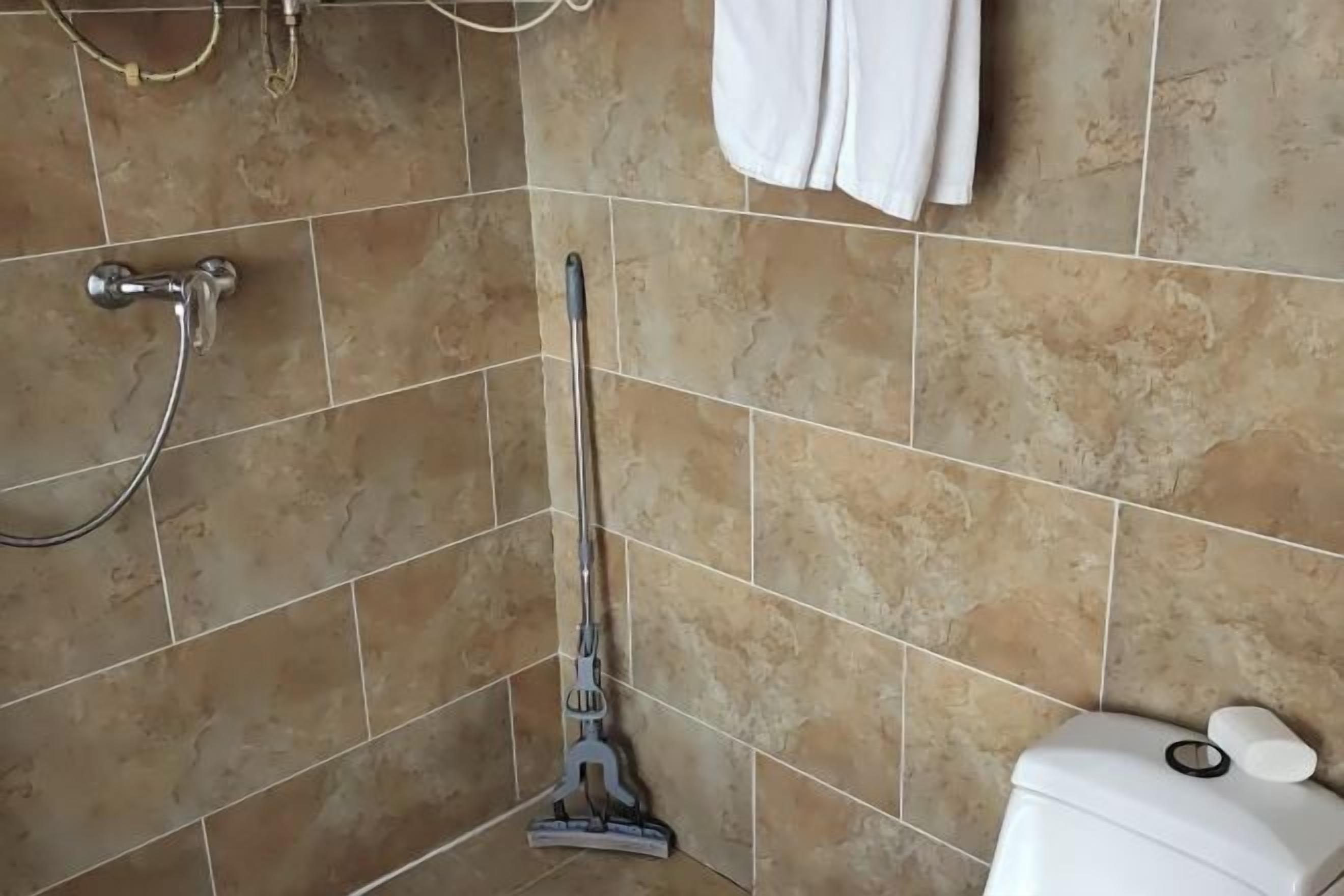A bathroom with a shower, a toilet, and a mop leaning against the wall.
