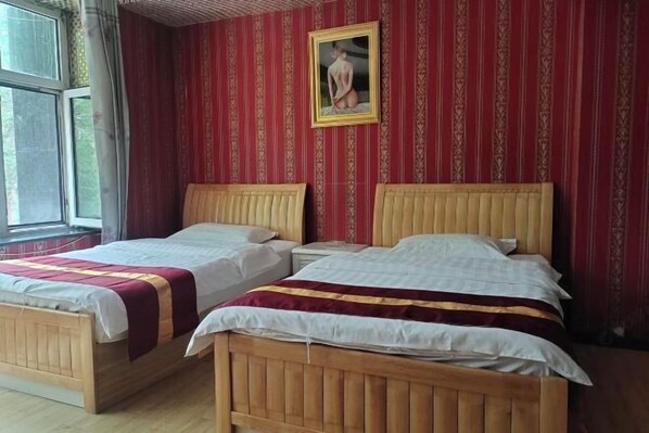 Dos camas de madera con ropa de cama blanca y burdeos, una ventana y un papel tapiz estampado.