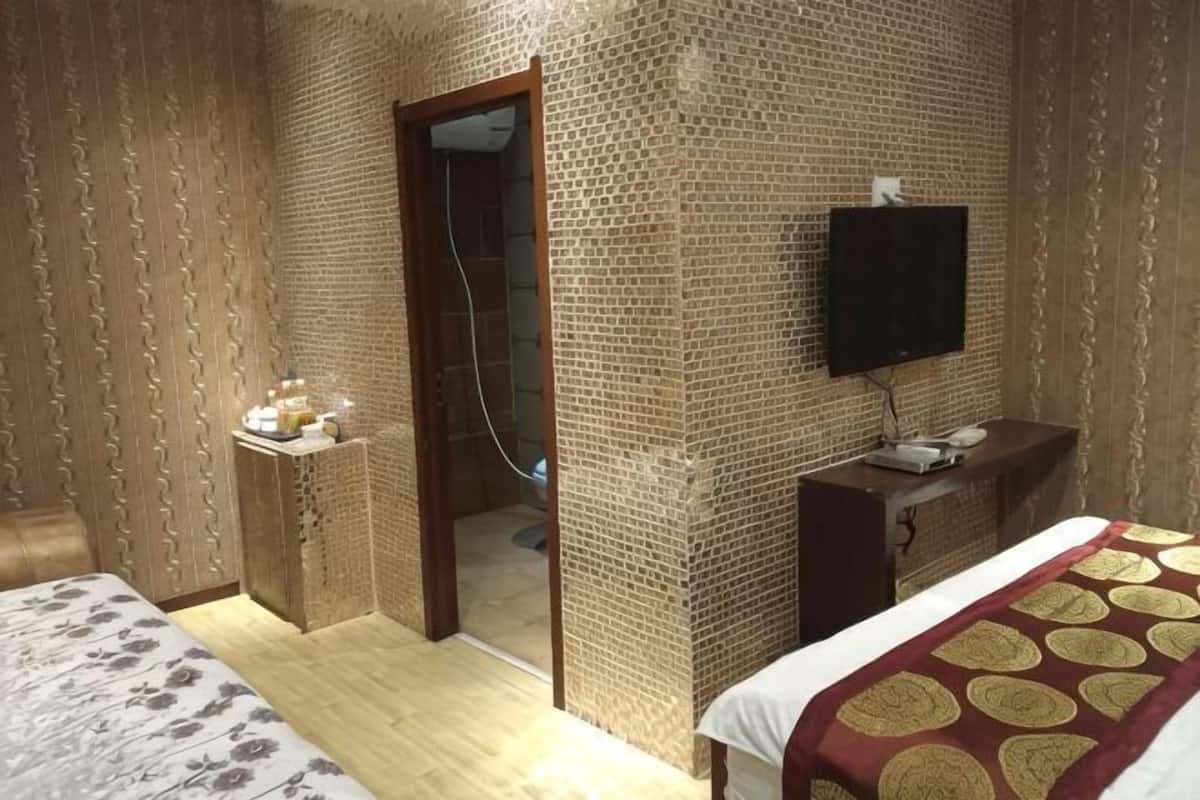 Quarto de hotel com cama, televisão, escrivaninha com computador e zona de chuveiro.