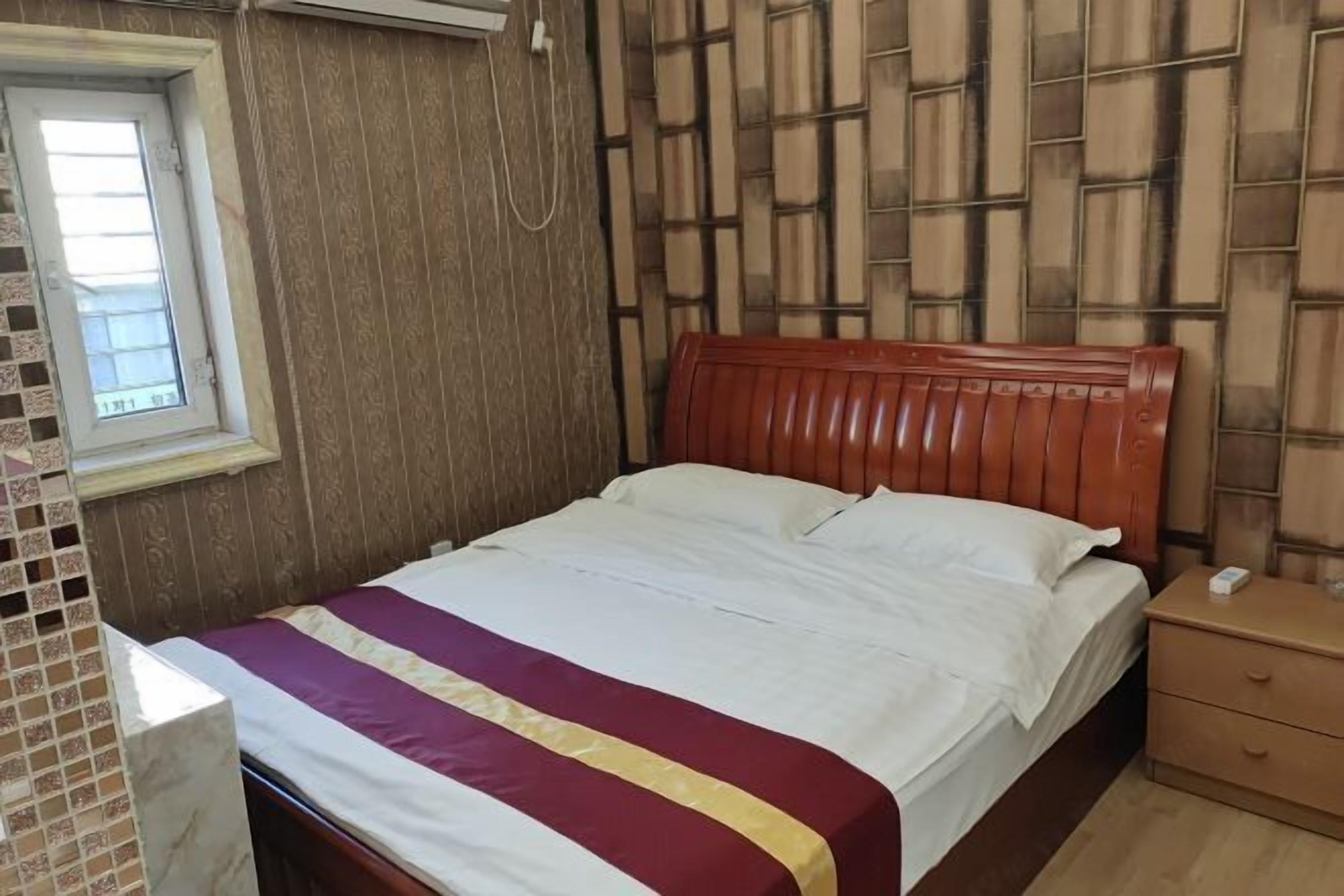 A single bed with a wooden headboard, a bedside table with a phone, and a window with a view of the outside.