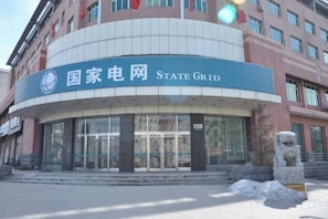 Un edificio con fachada curva, un letrero que dice 'State Grid' y una estatua de león de piedra en primer plano.