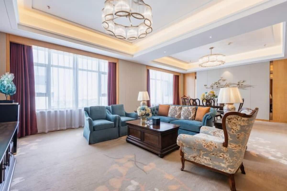 A spacious living room with a large window, a blue sofa, a patterned armchair, and a coffee table.