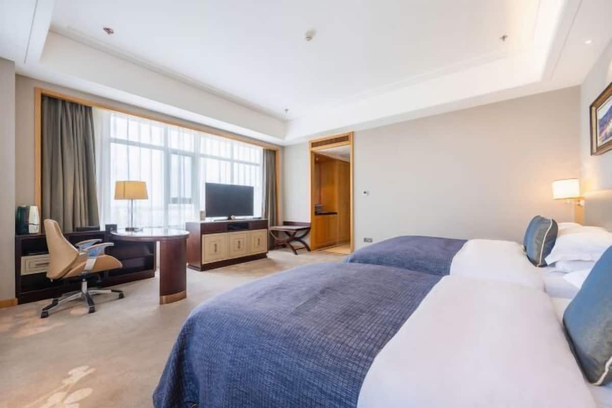 A hotel room with a bed, desk, chair, TV, and a view of the outside.