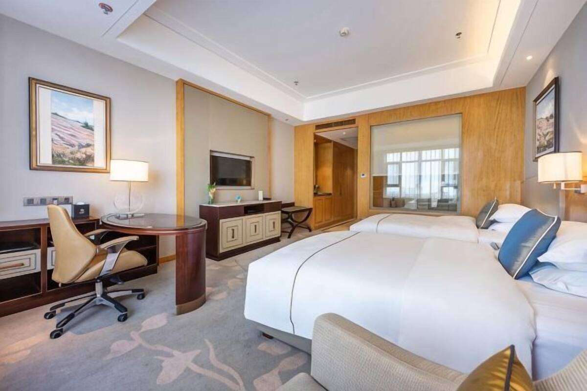 A hotel room with a large bed, a desk with a chair, a TV, and a bathroom visible through an open door.