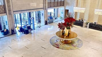 A lobby with a reception desk, seating area, and a decorative vase with red flowers.