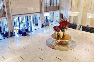 A lobby with a reception desk, seating area, and a decorative vase with red flowers.