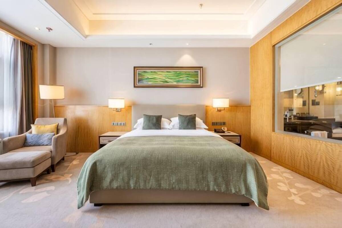 A hotel room with a large bed, two bedside tables, a chair, a large mirror, and a painting on the wall.