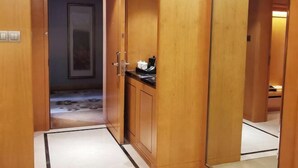 Un couloir en bois avec une porte donnant sur une pièce. On y trouve un petit meuble avec un plan de travail noir et un objet blanc posé dessus. Le sol est décoré d’un motif.