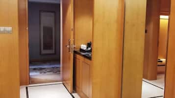 A wooden hallway with a door leading to a room. There is a small cabinet with a black countertop and a white object on it. The floor has a patterned design.