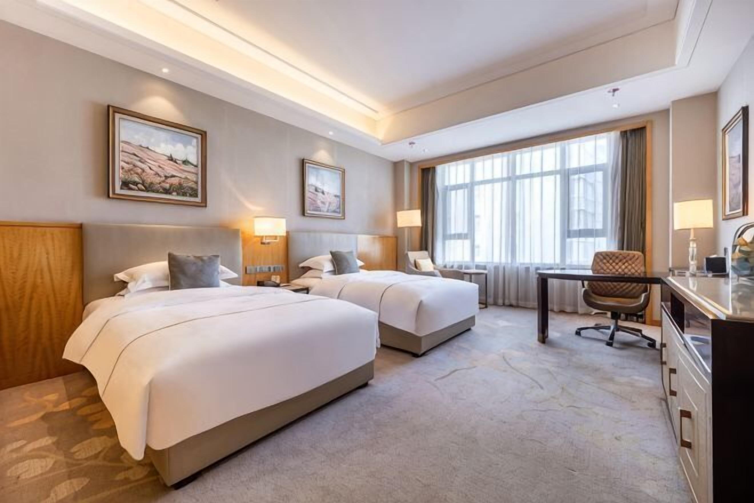 A hotel room with two beds, a desk, and a chair.