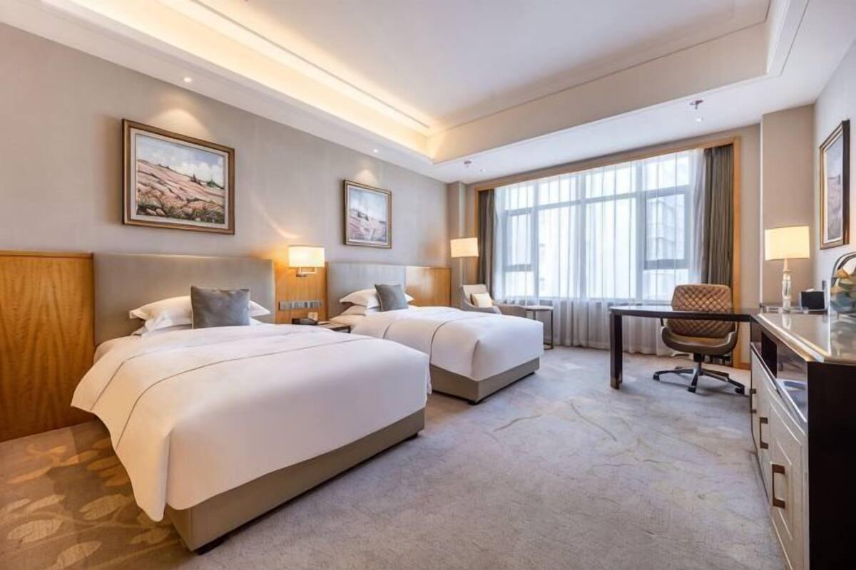 A hotel room with two beds, a desk, and a chair.
