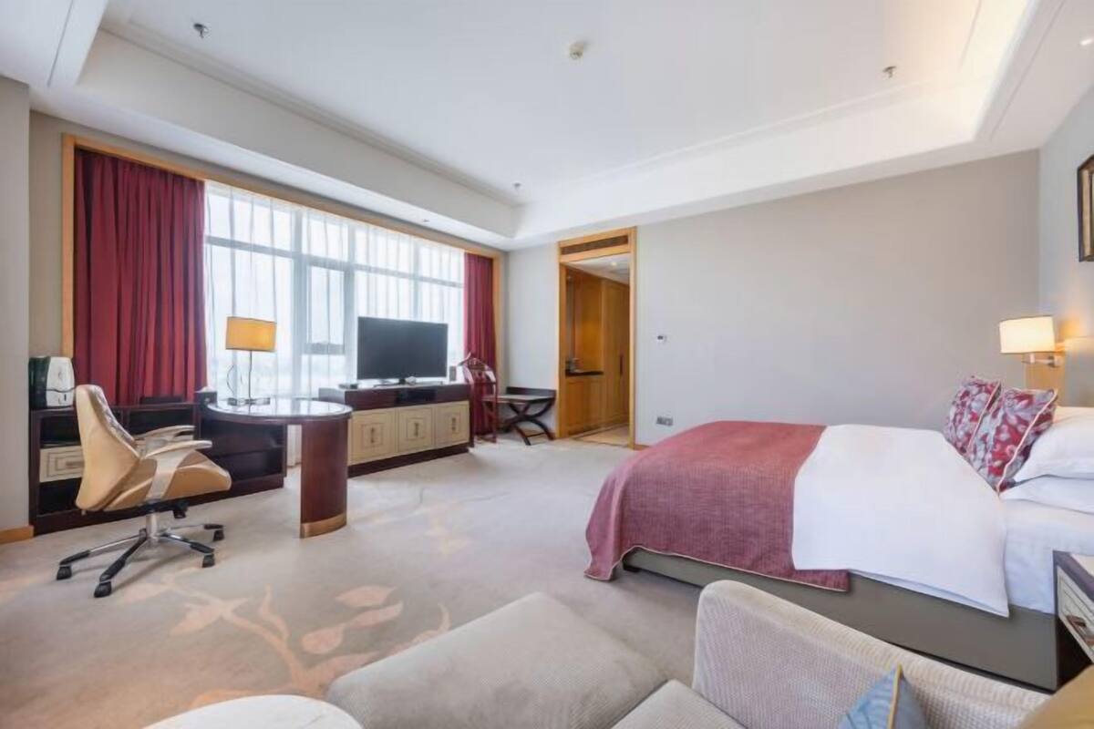 A hotel room with a bed, desk, chair, and a TV.