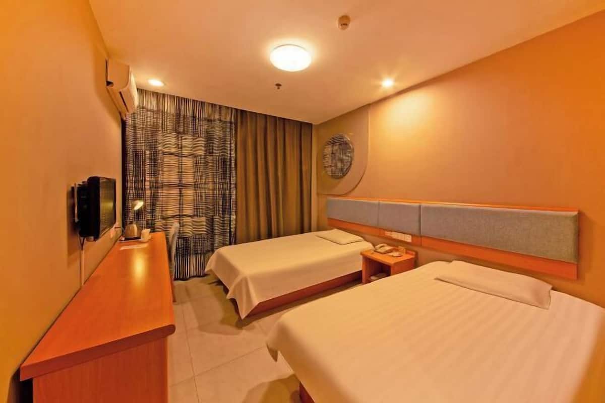 A hotel room with two beds, a desk, a telephone, and a wall-mounted TV.