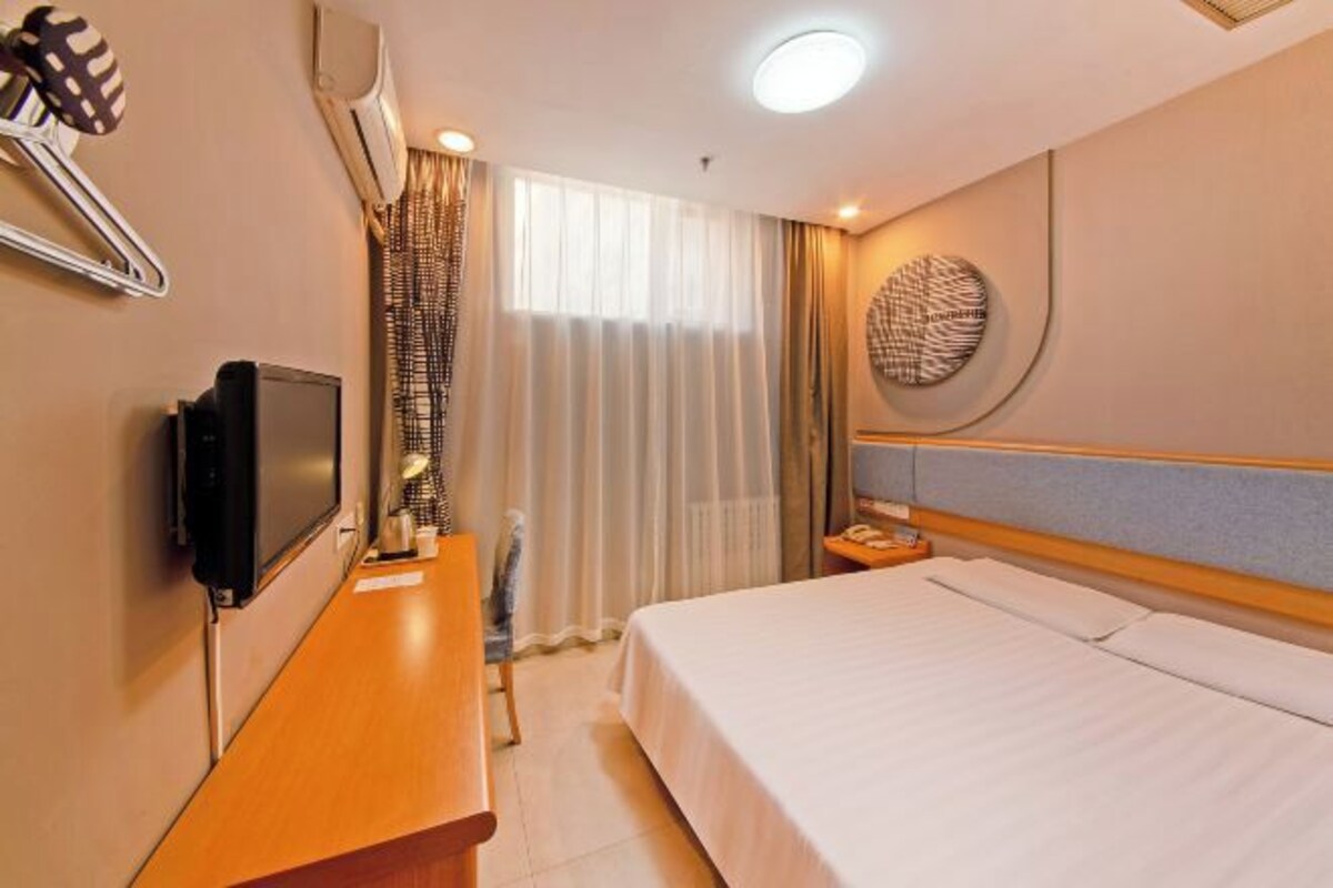 A hotel room with a bed, a TV, a desk, a chair, a nightstand, and a wall-mounted artwork.