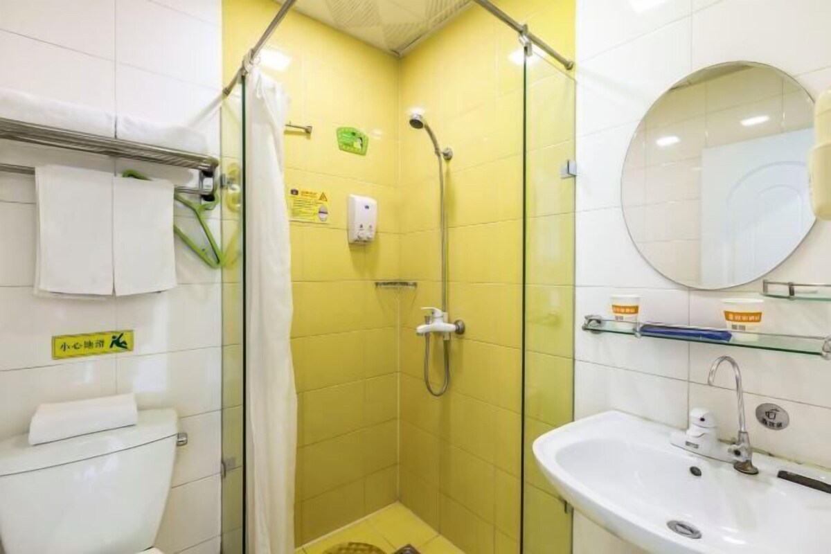 Ein Badezimmer mit gelben Fliesen, einer Duschkabine aus Glas, einem weißen Waschbecken und einem Spiegel.