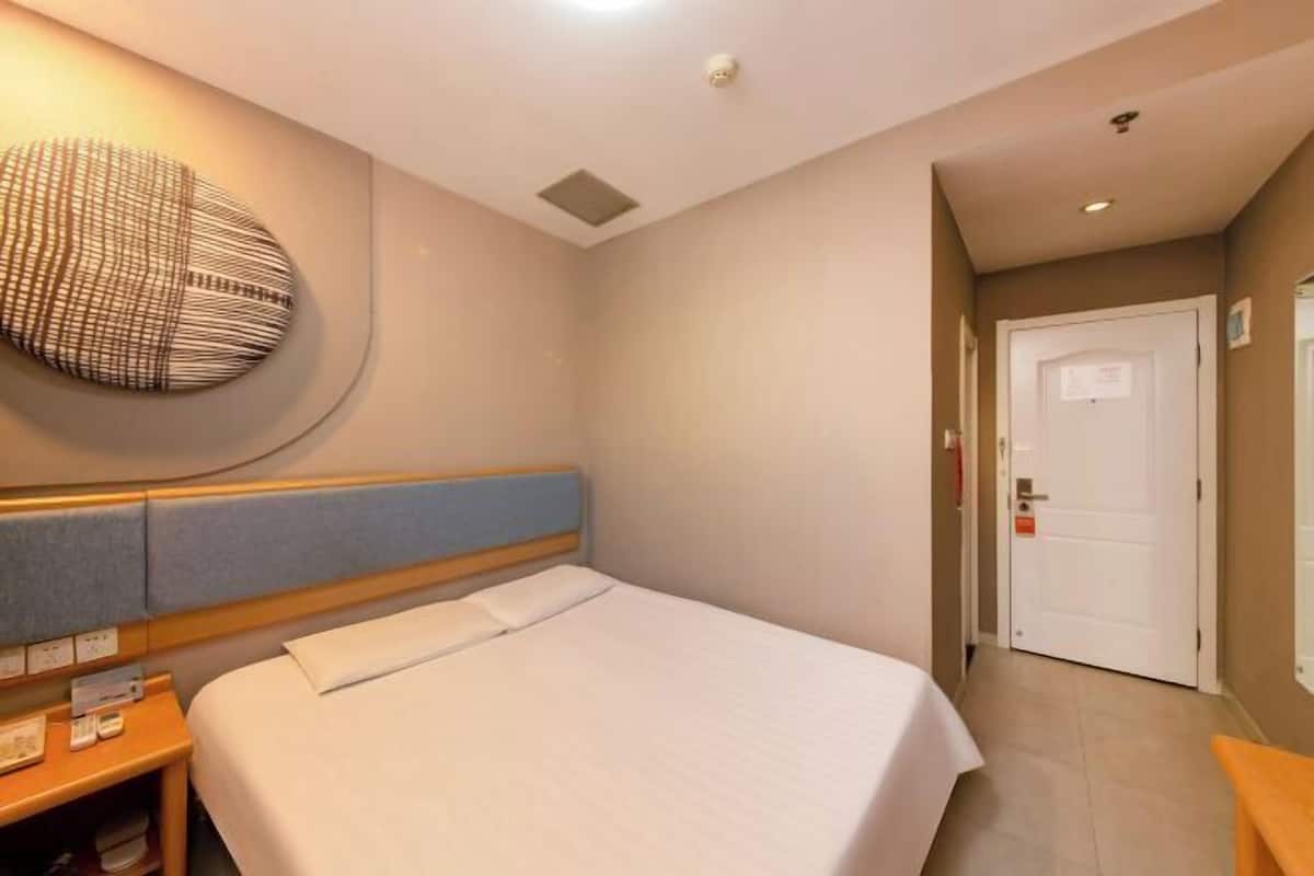 A hotel room with a bed, a bedside table, a wall-mounted artwork, a door, and a small bench.
