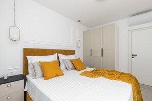 A neatly made bed with white bedding and a mustard-colored throw blanket, a wooden headboard, and a nightstand with drawers.