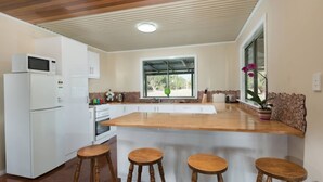 Una cucina moderna con mobili bianchi, un piano di lavoro in legno e un'ampia finestra. Si notano tre sgabelli in legno e un frigorifero.