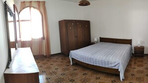 Ein Schlafzimmer mit Bett, Kleiderschrank, Schreibtisch und einem Fenster mit Vorhängen.