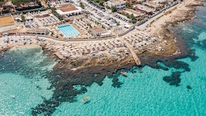 Luftaufnahme einer Küstenlandschaft mit Strand, Schwimmbad und felsiger Küste.