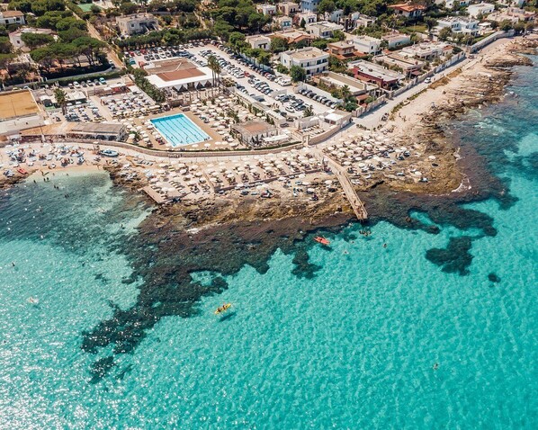 Vista aérea de una zona costera con playa, piscina y un litoral rocoso.