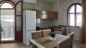 Eine Küche mit Kühlschrank, Holzschränken, einem Esstisch mit Korbstühlen und einer Topfpflanze.