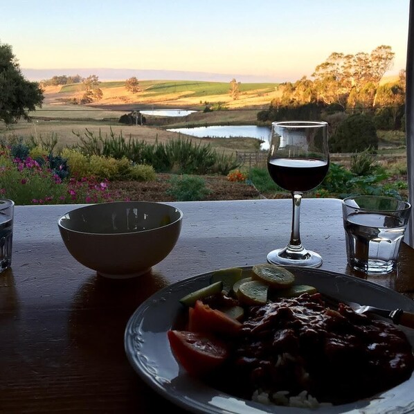 A table with a plate of food, a glass of red wine, and a view of a countryside landscape.