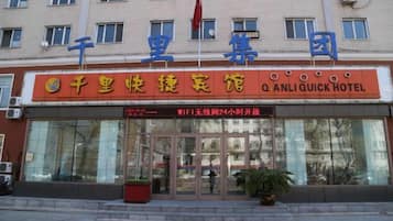 A hotel entrance with a sign reading 'Q Anli Quick Hotel' and a flag above it.