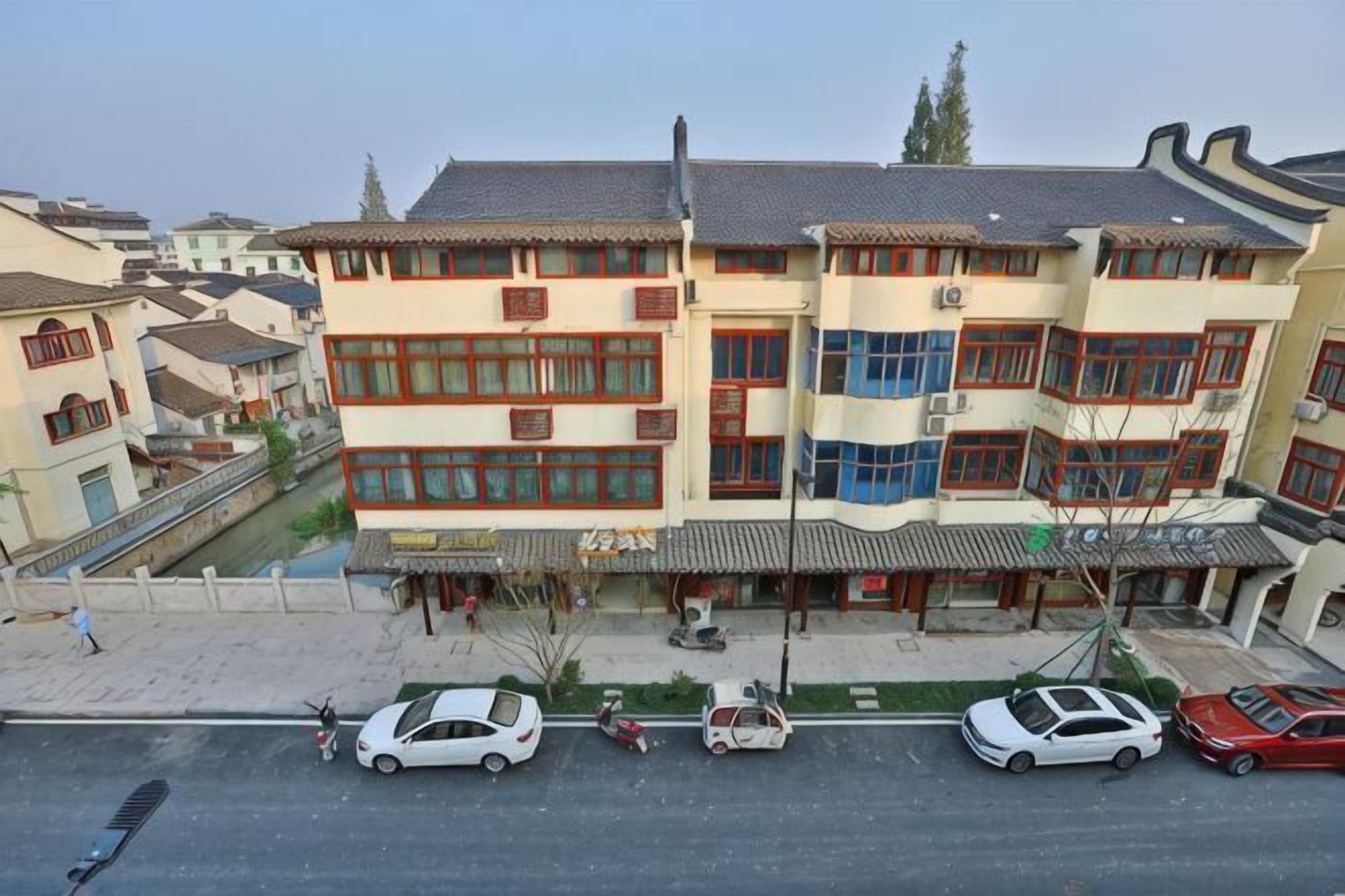 Un immeuble à plusieurs étages, de style architectural traditionnel, doté d’une cour intérieure et d’une rangée de voitures garées le long de la rue.