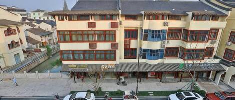 Un immeuble à plusieurs étages, de style architectural traditionnel, doté d’une cour intérieure et d’une rangée de voitures garées le long de la rue.