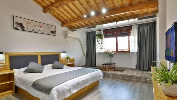 A bedroom with a wooden ceiling, a bed with grey bedding, a bedside table, a TV, and a window with curtains. - Meitu Huashe Guesthouse (Tongxiang)