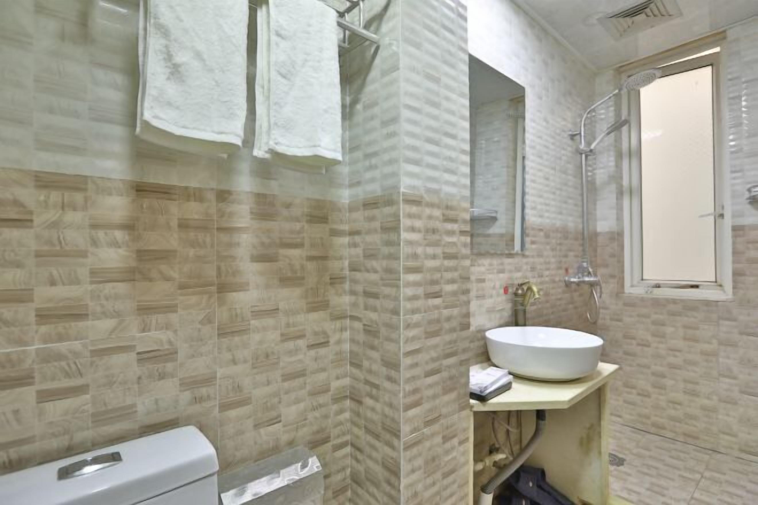 A bathroom with a tiled wall, a sink, a shower, and a toilet.