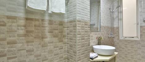 A bathroom with a tiled wall, a sink, a shower, and a toilet.