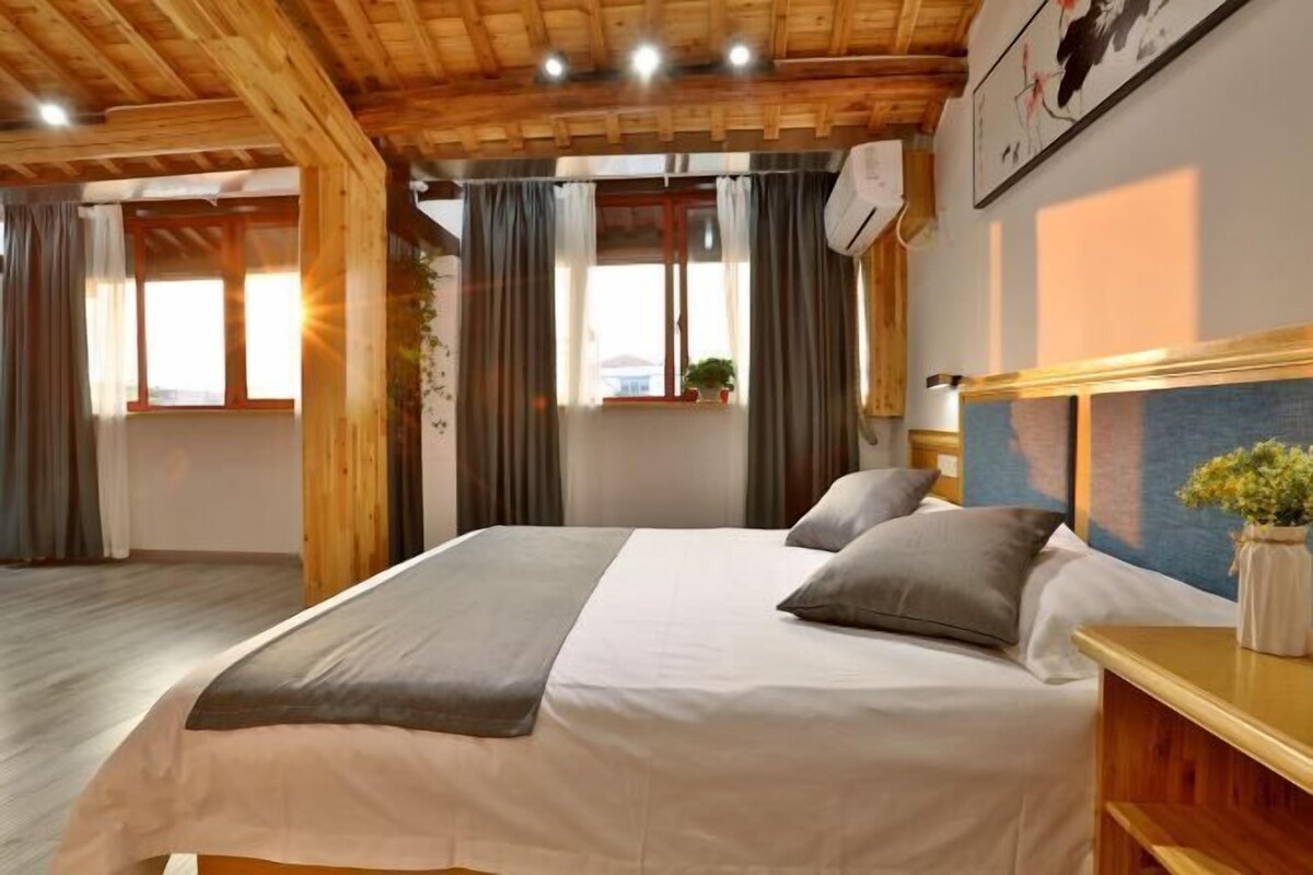 Een slaapkamer met een bed, gordijnen, een raam, een plant en een luchtverkoeler aan de muur.