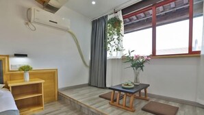 A room with a bed, a small wooden table with a vase, a bench, and a window with curtains. - Meitu Huashe Guesthouse (Tongxiang)
