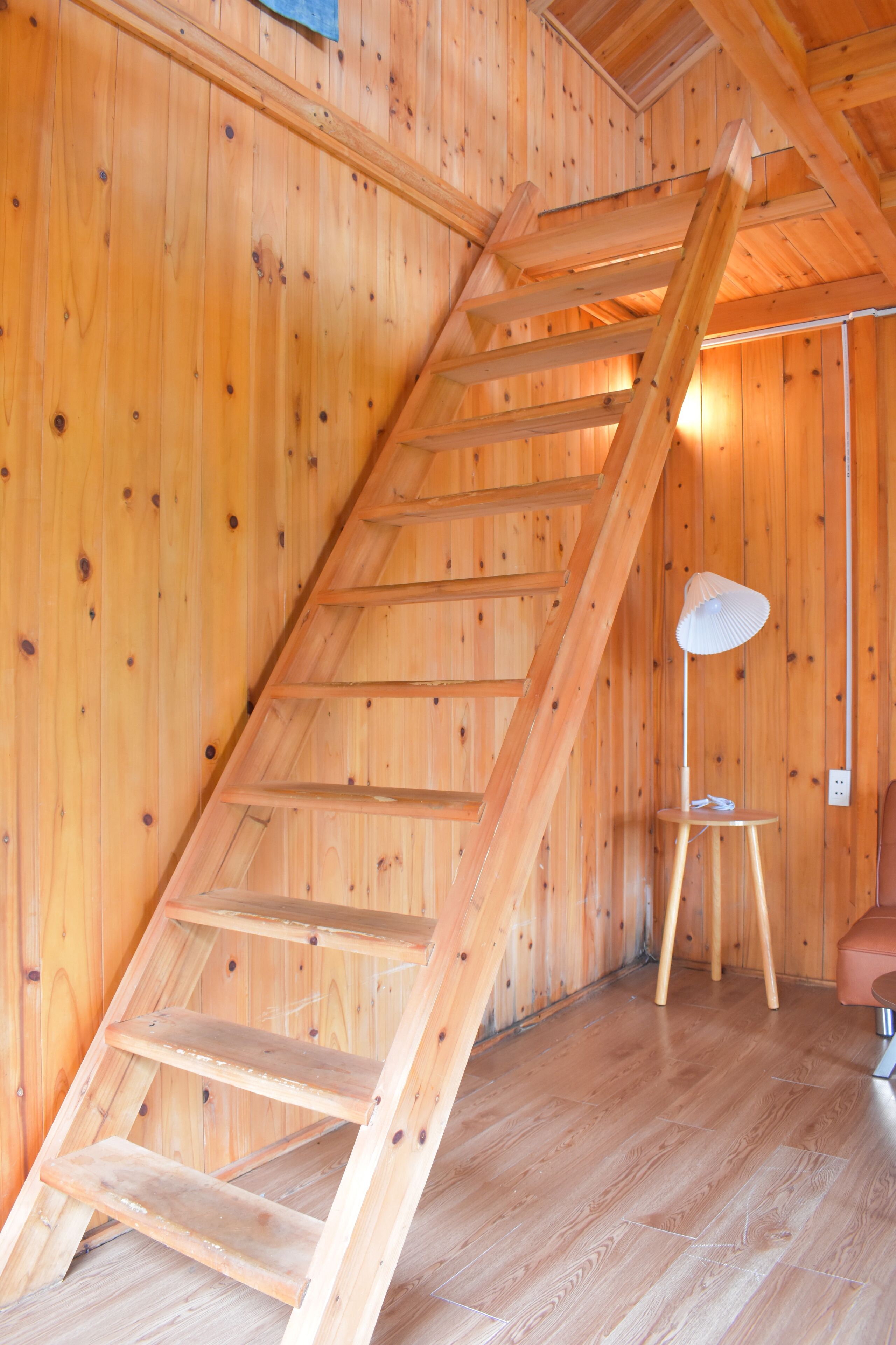 A wooden interior with a wooden staircase, a small round table with a lamp, and a wooden bench.